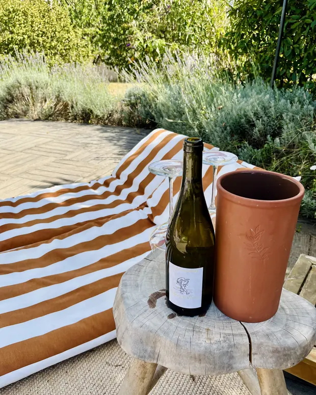 Une bouteille de vin blanc et un seau en terre cuite sur un tabouret, au bord de la piscine
