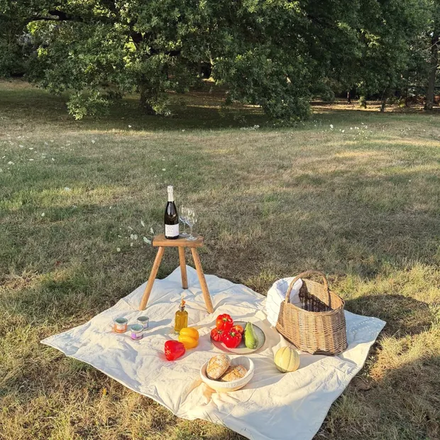 Une nappe blanche dressée dans l'herbe du verger : fromages, pain, légumes du jardin et une bouteille de vin sur un tabouret