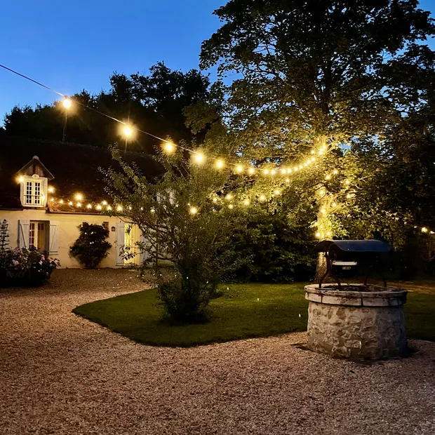 La cour de gravier et son puits de pierre, éclairés par les guirlandes à la nuit tombante