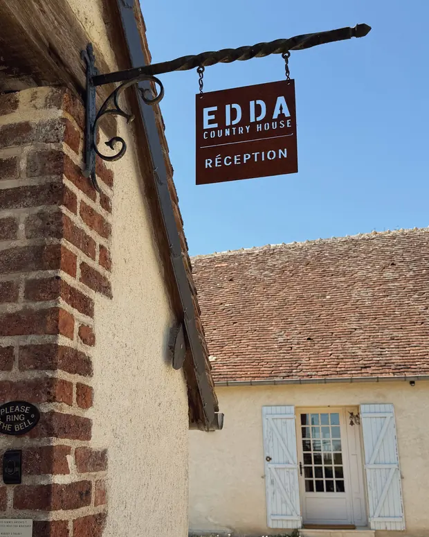 L'enseigne EDDA Country House en fer forgé, accrochée au mur de brique
