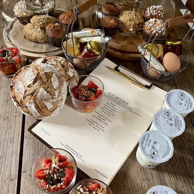 Un petit-déjeuner complet dressé sur une table en bois : pain au levain, brioche, cookies, yaourts, salade de fruits et la carte EDDA