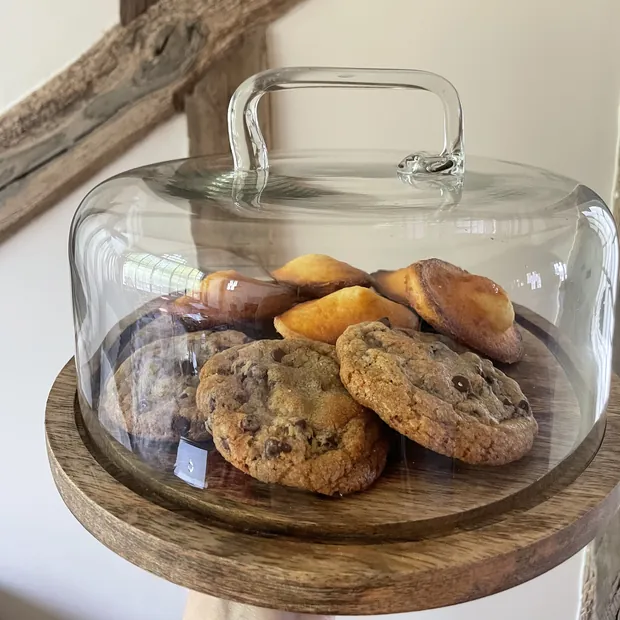 Des cookies et des muffins maison sous une cloche de verre, sur un plateau de bois